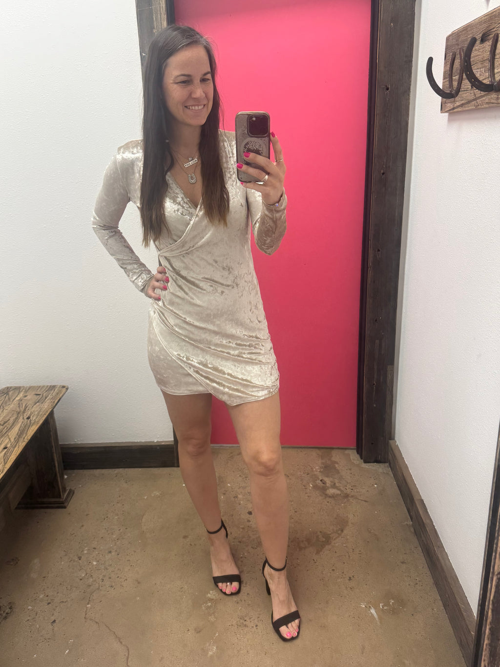 Person taking a mirror selfie wearing a silver dress in a room with pink wall and wooden floor.