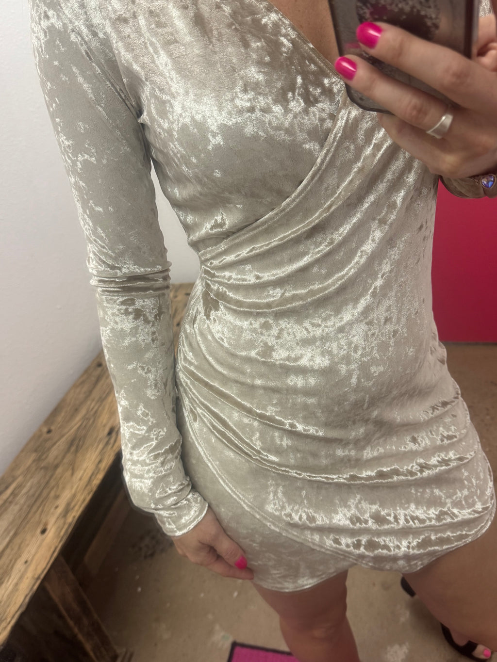 Person taking a mirror selfie wearing a silver dress in a room with pink wall and wooden floor.