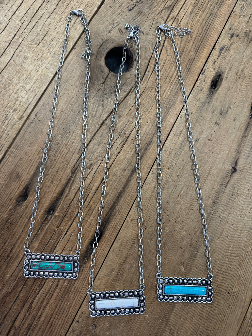 Three silver bar necklaces with blue and white gemstone inlays, displayed on a wooden surface.
