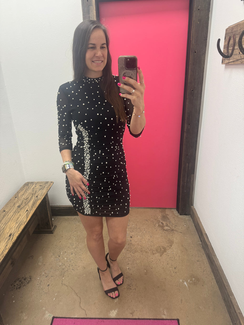 Person taking a mirror selfie wearing a black dress with white polka dots in a room with pink walls.